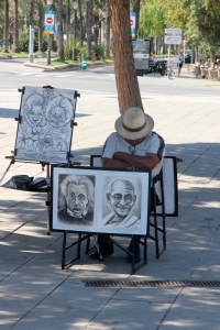 Karikatuur tekenaar slaapt achter zijn potloodtekeningen van Einstein en Ghandi.